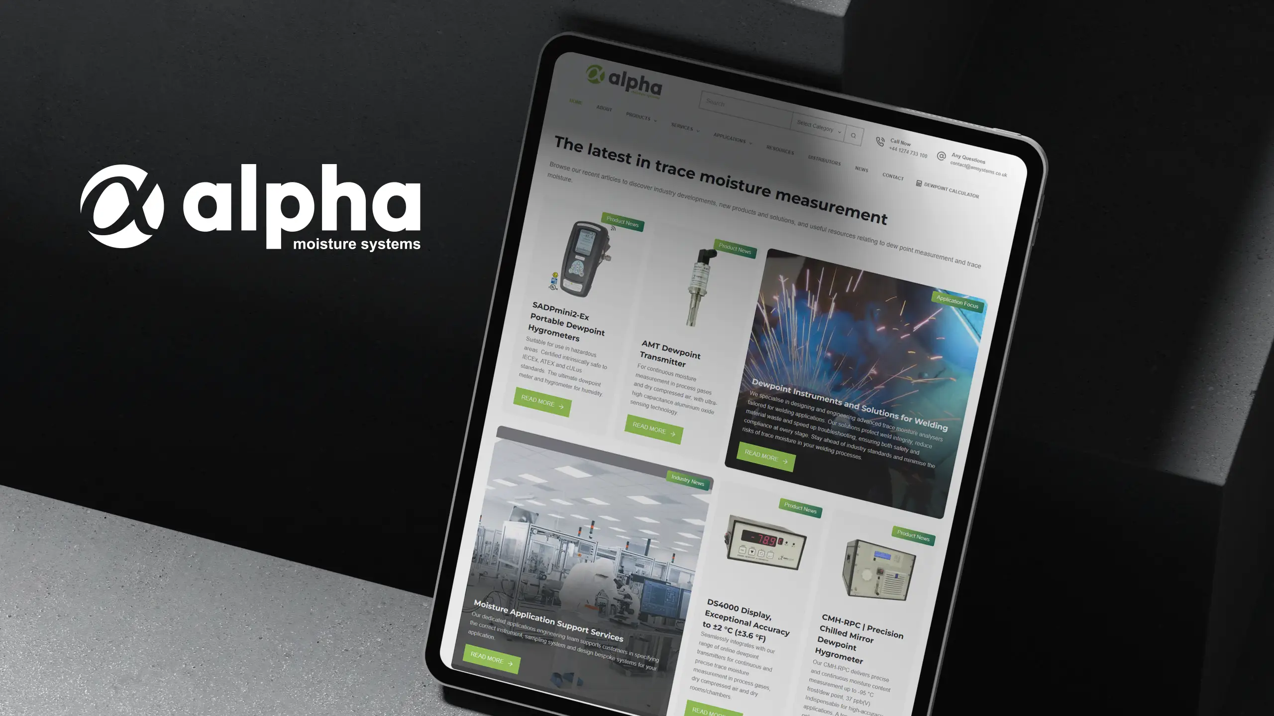 Alpha Moisture Systems website presented on three screens in a concrete studio setting