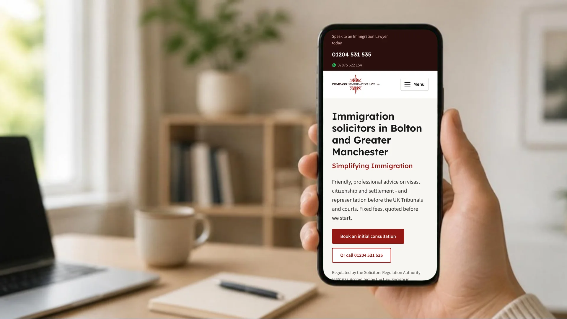 A hand holding a phone showing the Compass Immigration Law homepage, with the office number, WhatsApp number and book a consultation button above the fold