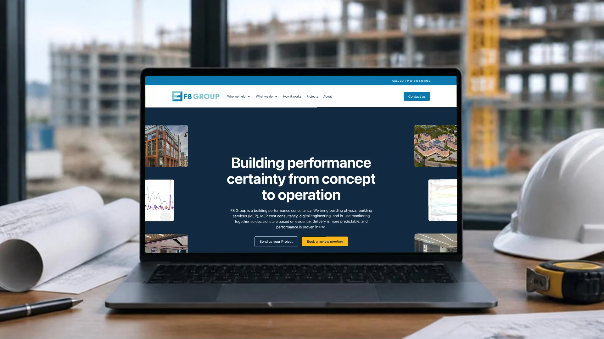A laptop on a site office desk beside a hard hat and drawings, showing the F8 Group homepage: 'Building performance certainty from concept to operation'