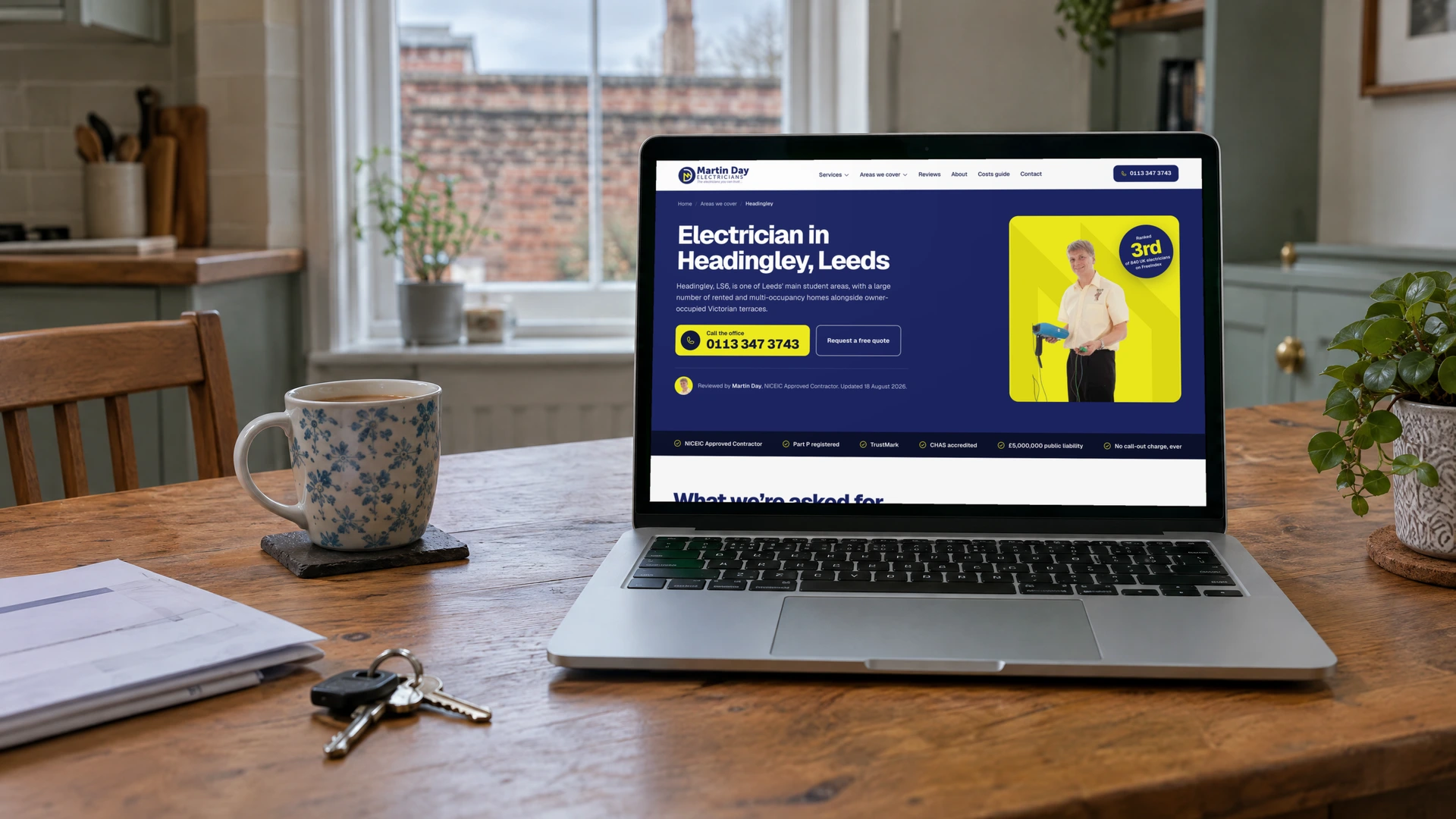 A laptop on a kitchen table showing the Martin Day Electricians Headingley page, with a local introduction, call and quote buttons and a reviewed-by line naming Martin